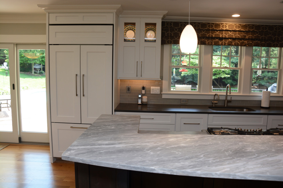 Photo of a large transitional l-shaped open plan kitchen in Baltimore with an undermount sink, recessed-panel cabinets, white cabinets, granite benchtops, grey splashback, panelled appliances, medium hardwood floors, with island, brown floor and black benchtop.