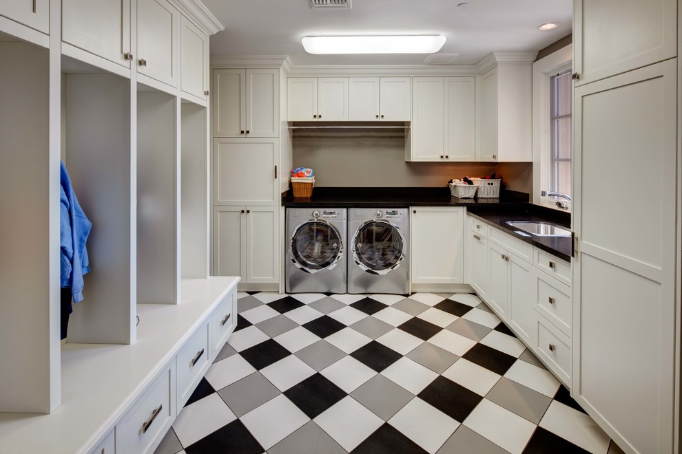 Mid-sized mediterranean u-shaped utility room in Phoenix with an undermount sink, recessed-panel cabinets, white cabinets, quartz benchtops, beige walls, vinyl floors, a side-by-side washer and dryer, multi-coloured floor and black benchtop.