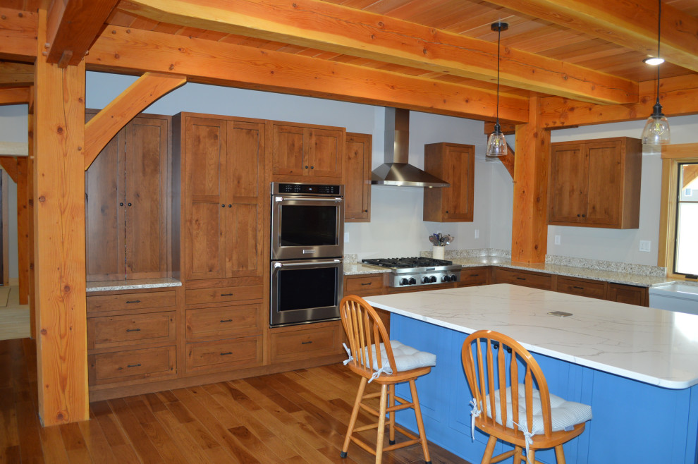 Example of a mid-sized mountain style u-shaped medium tone wood floor, brown floor and exposed beam eat-in kitchen design with a farmhouse sink, shaker cabinets, medium tone wood cabinets, paneled appliances and an island