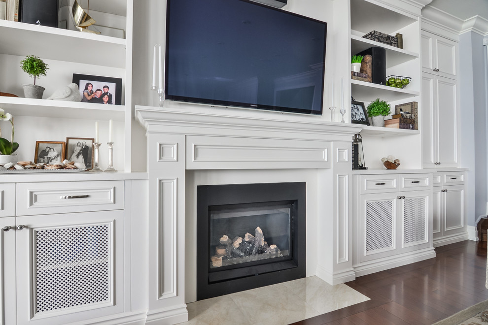 Photo of a large traditional enclosed family room in Toronto with white walls, medium hardwood floors, a standard fireplace, a wood fireplace surround and a wall-mounted tv.
