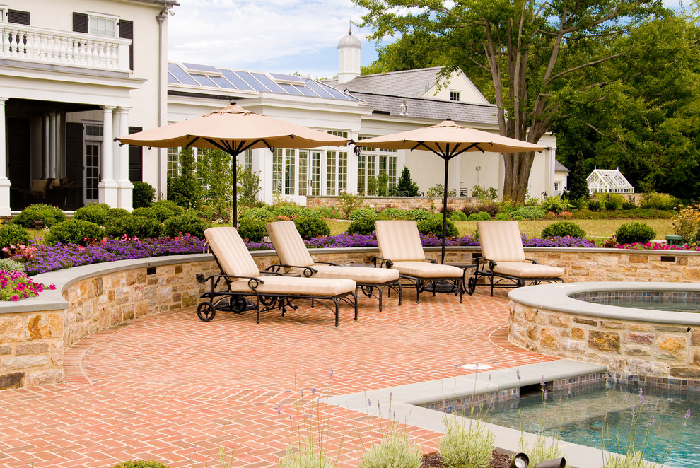 Large traditional backyard custom-shaped lap pool in Philadelphia with brick pavers and a hot tub.