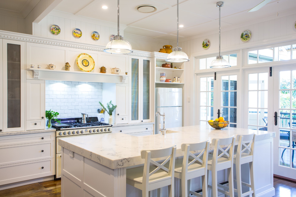 Photo of a large traditional galley eat-in kitchen in Brisbane with shaker cabinets, white cabinets, white splashback, with island, subway tile splashback, dark hardwood floors, white appliances and marble benchtops.