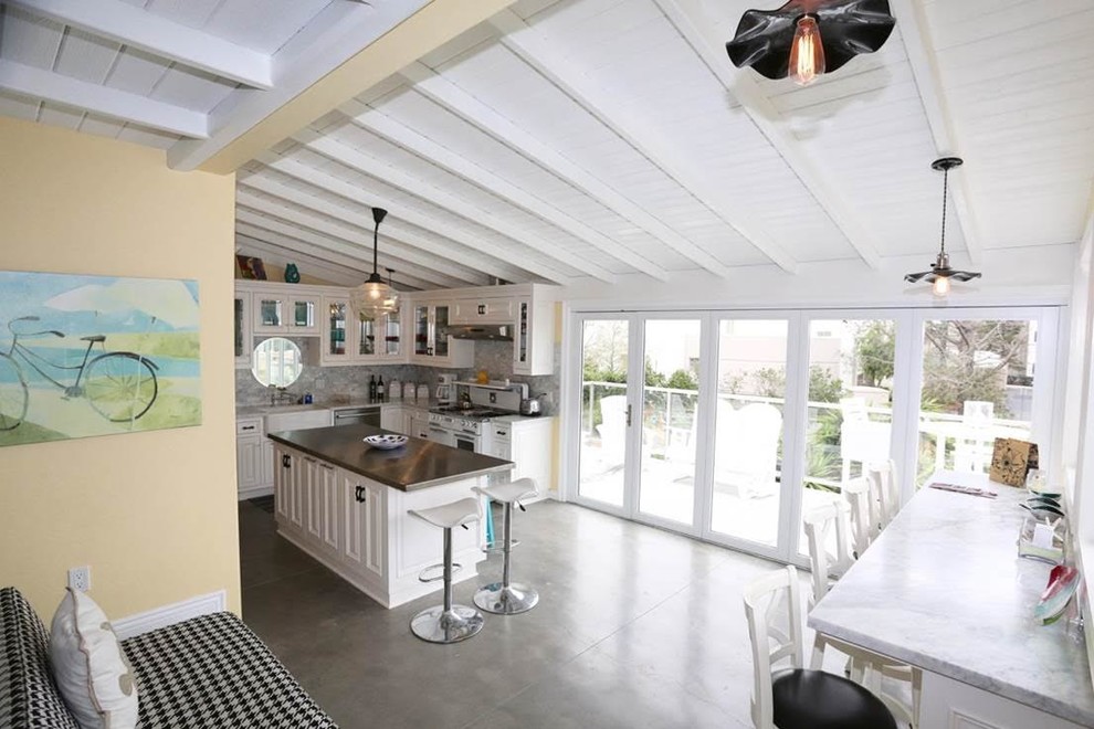 Inspiration for a mid-sized beach style l-shaped eat-in kitchen in Orange County with beaded inset cabinets, white cabinets, quartzite benchtops, white splashback, stone tile splashback, white appliances, concrete floors, with island and brown floor.