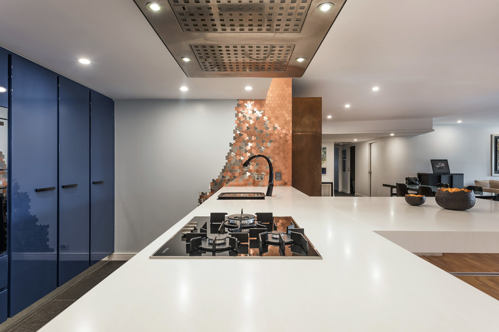 This is an example of a large contemporary galley eat-in kitchen in Sydney with an integrated sink, flat-panel cabinets, blue cabinets, solid surface benchtops, metallic splashback, metal splashback, black appliances, light hardwood floors, with island and brown floor.