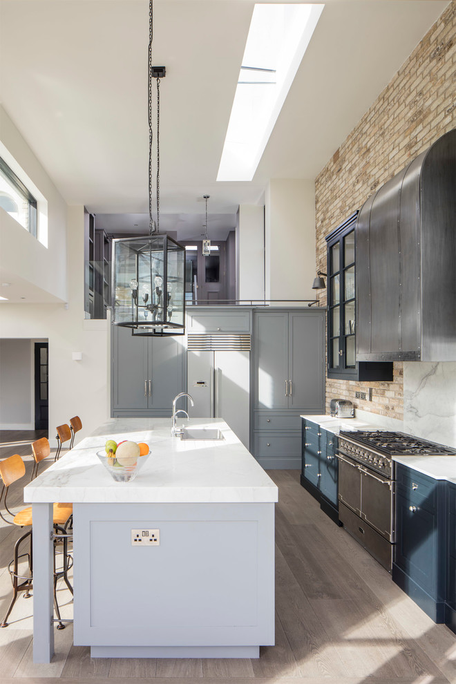 This is an example of a mid-sized industrial eat-in kitchen in Dublin with an undermount sink, shaker cabinets, grey cabinets, marble benchtops, stone slab splashback, stainless steel appliances, medium hardwood floors and with island.