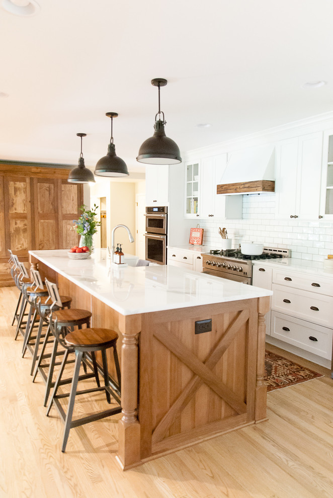 Design ideas for a country galley kitchen in Houston with shaker cabinets, with island, white cabinets, white splashback, subway tile splashback, stainless steel appliances, light hardwood floors and beige floor.