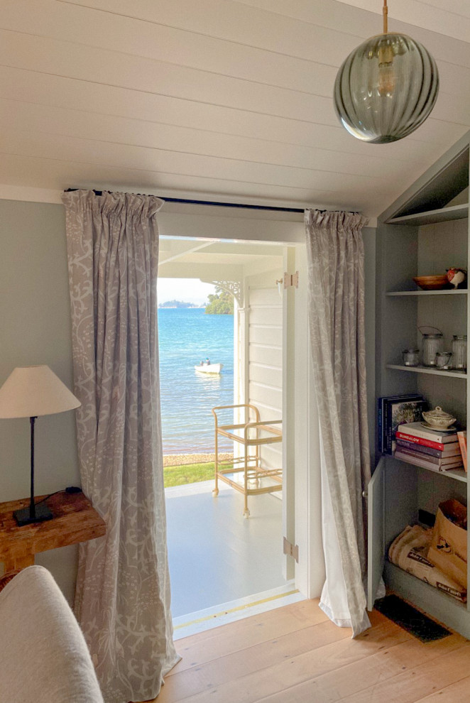 Design ideas for a Mid-sized beach style Open Concept living room in Auckland With Blue Walls, Light Hardwood Floors, a Wood Stove, a Stone Fireplace Surround, a Built-in Media Wall and Wood Walls.