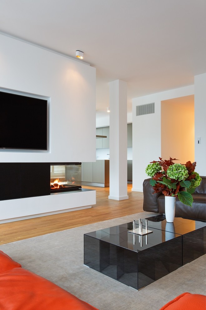 Photo of a large contemporary formal open concept living room in Berlin with medium hardwood floors, a two-sided fireplace, white walls, a wall-mounted tv, a plaster fireplace surround and beige floor.