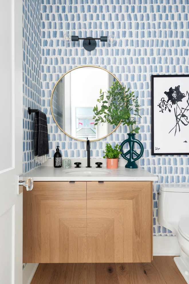Photo of a medium sized beach style cloakroom in Minneapolis with light wood cabinets, a one-piece toilet, blue walls, medium hardwood flooring, a submerged sink, engineered stone worktops, a floating vanity unit and wallpapered walls.