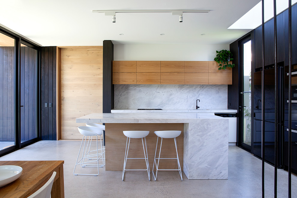 Photo of a mid-sized contemporary eat-in kitchen in Melbourne with with island, flat-panel cabinets, medium wood cabinets, white splashback, concrete floors, grey floor and white benchtop.