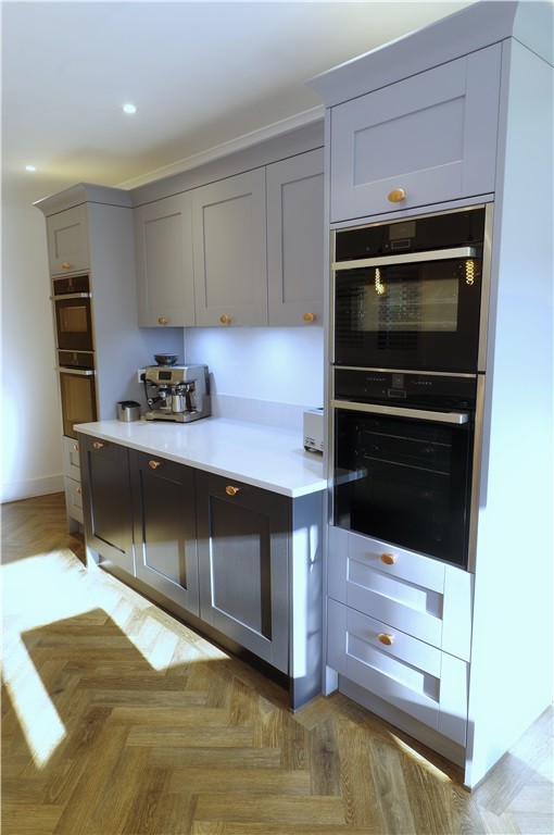 Modern galley eat-in kitchen in Kent with grey cabinets, quartzite benchtops, white splashback, black appliances, brown floor and grey benchtop.