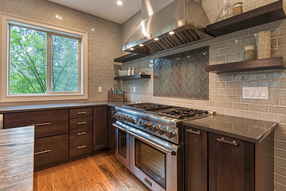 Example of a large transitional l-shaped medium tone wood floor and brown floor open concept kitchen design with a farmhouse sink, shaker cabinets, dark wood cabinets, granite countertops, gray backsplash, subway tile backsplash, paneled appliances and an island