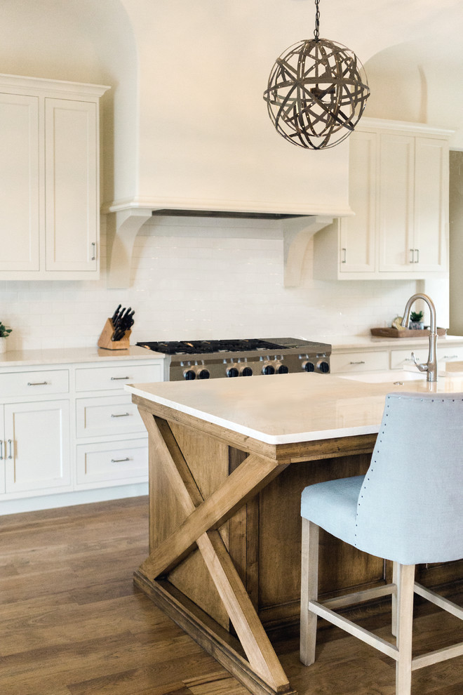 Mid-sized transitional medium tone wood floor and brown floor open concept kitchen photo in Nashville with a farmhouse sink, beaded inset cabinets, white cabinets, marble countertops, white backsplash, ceramic backsplash, white appliances and an island
