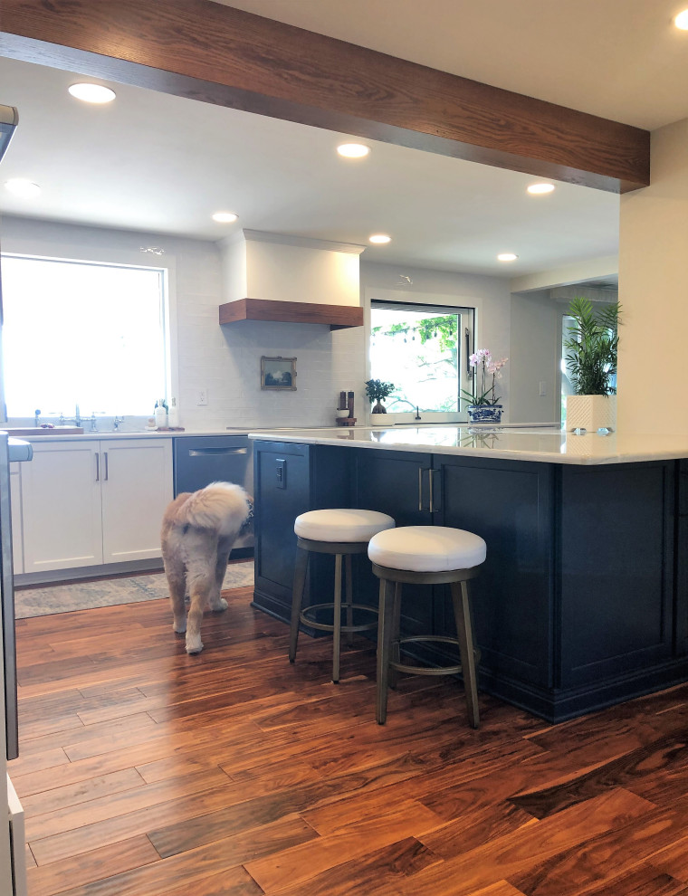 Inspiration for a mid-sized transitional l-shaped medium tone wood floor and brown floor kitchen pantry remodel with an undermount sink, flat-panel cabinets, blue cabinets, quartz countertops, white backsplash, subway tile backsplash, stainless steel appliances, an island and gray countertops