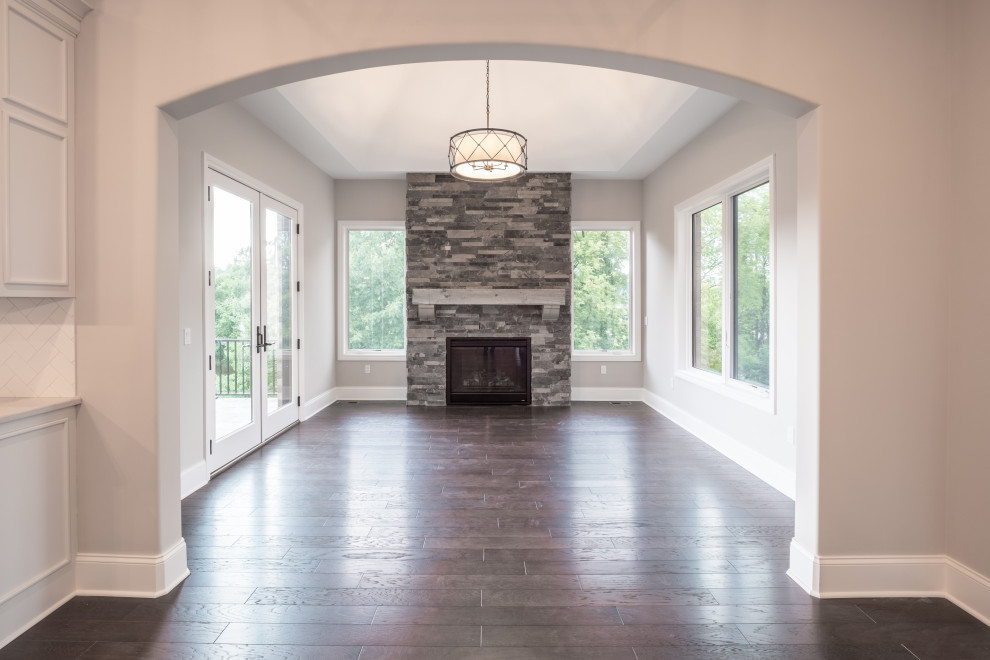 Large country enclosed living room in Detroit with beige walls, dark hardwood floors, a standard fireplace, a stone fireplace surround and brown floor.