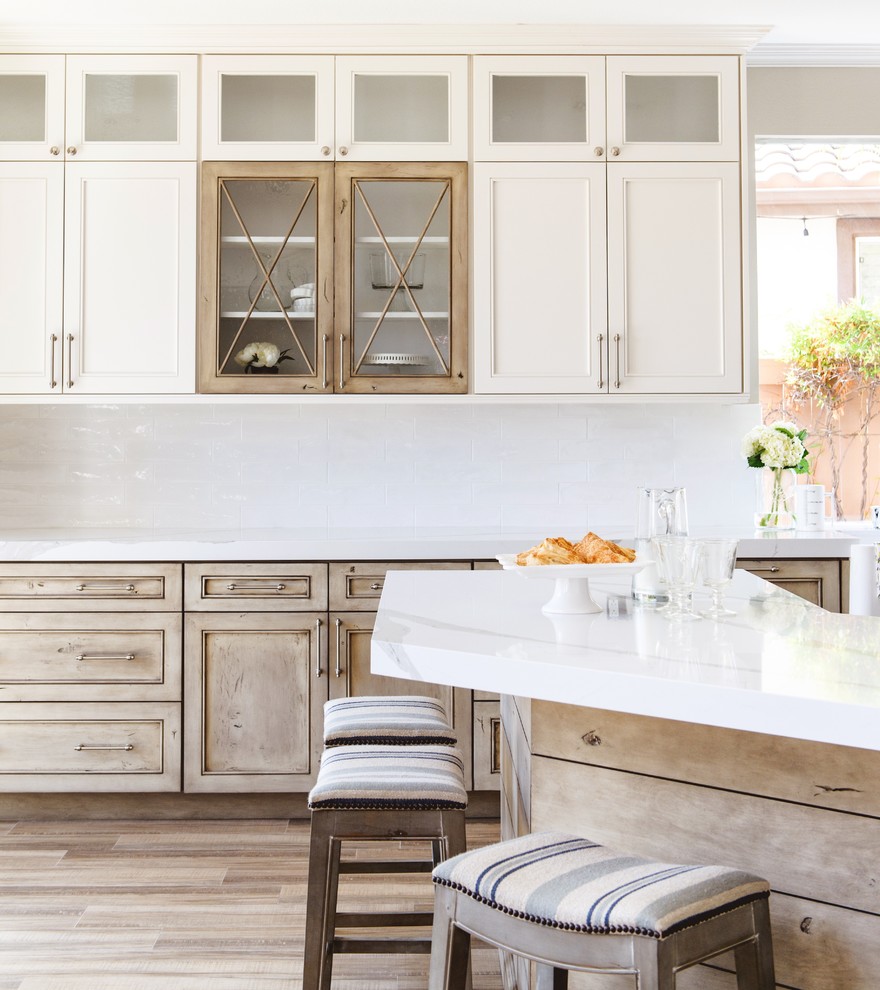 Inspiration for a mid-sized transitional open plan kitchen in San Diego with a farmhouse sink, shaker cabinets, white cabinets, quartzite benchtops, white splashback, stainless steel appliances, medium hardwood floors, a peninsula and brown floor.
