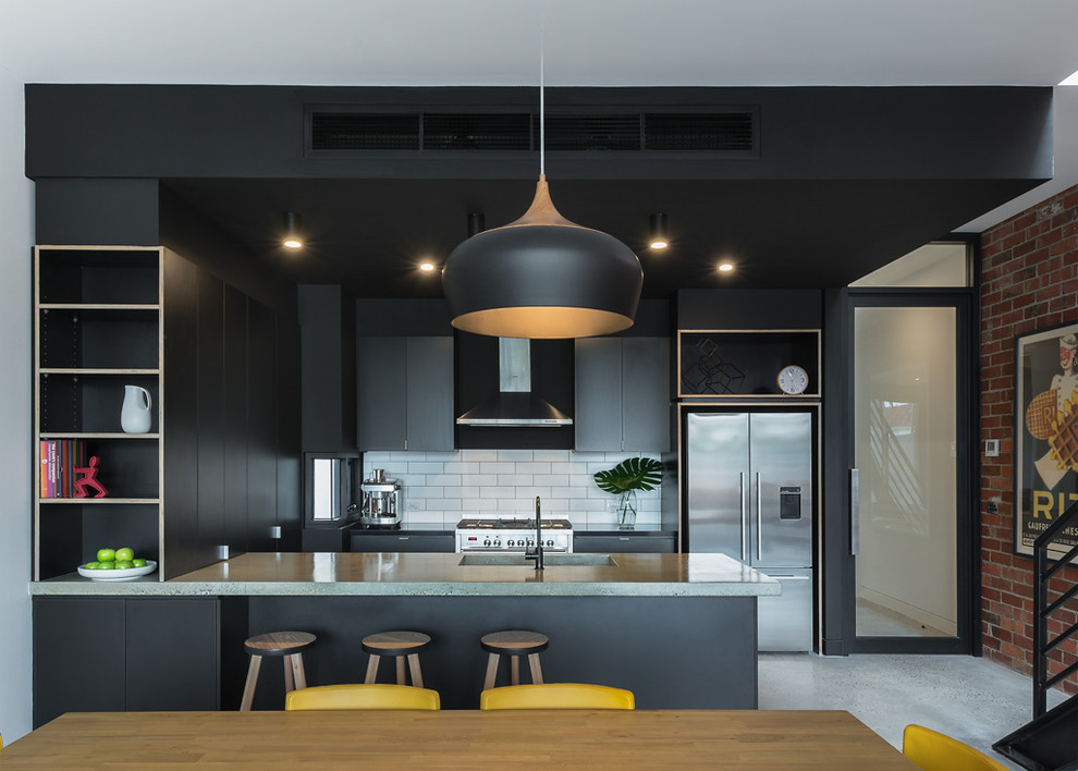 This is an example of a small industrial u-shaped open plan kitchen in Melbourne with an integrated sink, black cabinets, concrete benchtops, white splashback, subway tile splashback, stainless steel appliances, concrete floors and a peninsula.