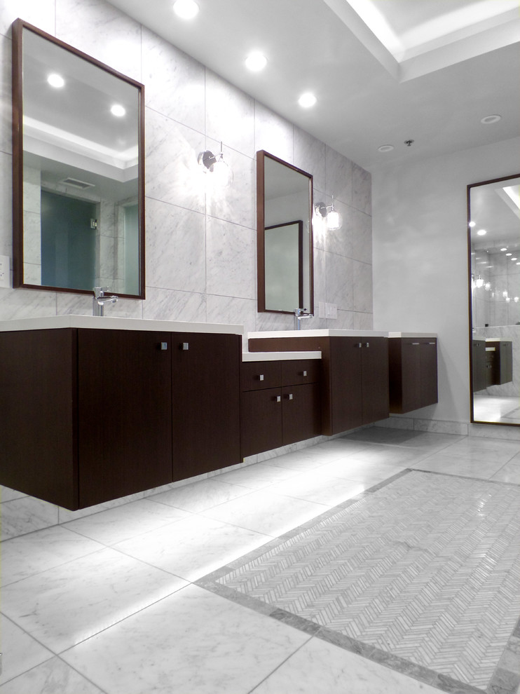 Photo of a large modern bathroom in Los Angeles with an undermount sink, flat-panel cabinets, dark wood cabinets, solid surface benchtops, a one-piece toilet, grey walls, marble floors, gray tile, marble and grey floor.