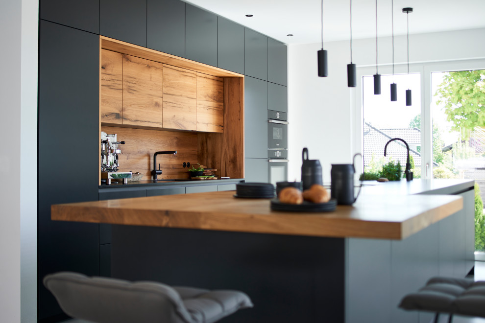 Design ideas for a contemporary kitchen in Munich with flat-panel cabinets, black cabinets, granite benchtops, black appliances, concrete floors, with island, grey floor and grey benchtop.