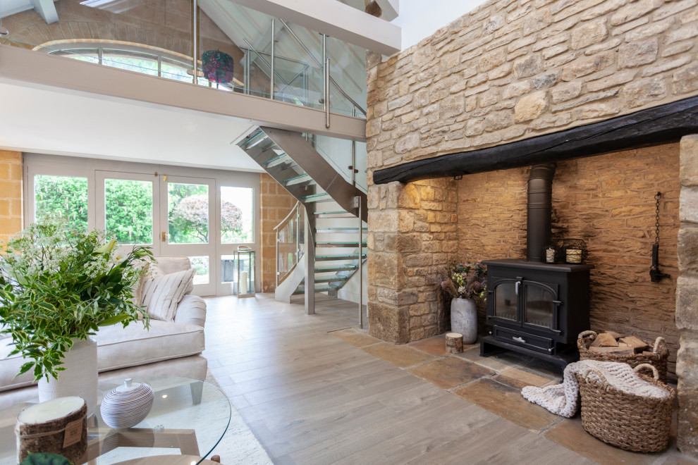 Inspiration for a large country loft-style living room in Gloucestershire with white walls, vinyl floors, a wood stove, a stone fireplace surround, a concealed tv and exposed beam.
