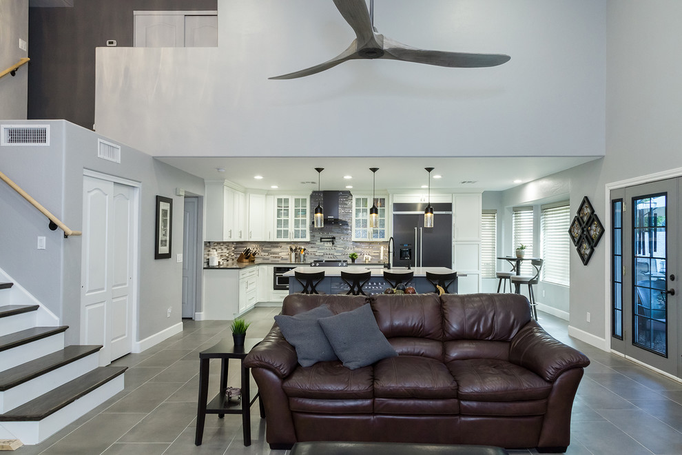 Inspiration for a mid-sized transitional l-shaped porcelain tile and gray floor open concept kitchen remodel in Phoenix with an undermount sink, shaker cabinets, white cabinets, quartz countertops, gray backsplash, glass tile backsplash, black appliances, an island and gray countertops