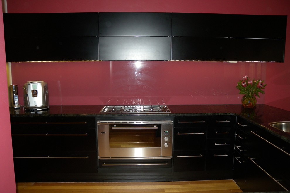 Inspiration for a contemporary kitchen in Adelaide with a drop-in sink, black cabinets, granite benchtops, glass sheet splashback, stainless steel appliances and medium hardwood floors.