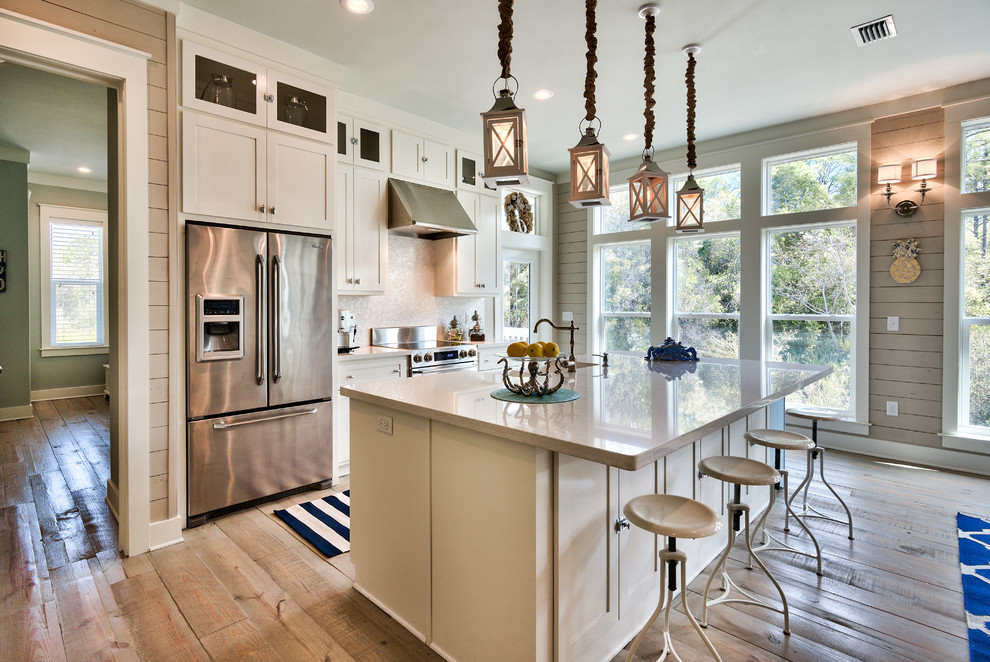 This is an example of a beach style galley kitchen in Miami with shaker cabinets, white cabinets, white splashback, stainless steel appliances, medium hardwood floors and with island.