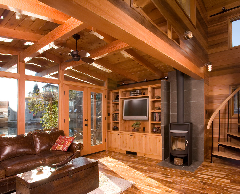 Photo of a country open concept living room in Seattle with a stone fireplace surround, a wood stove, medium hardwood floors and a wall-mounted tv.