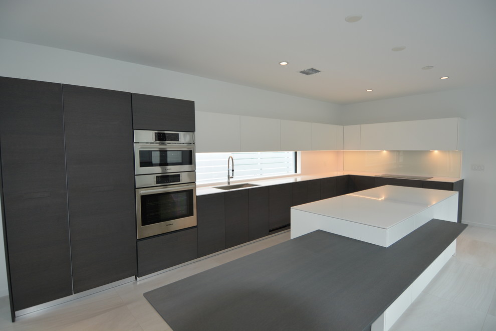 This is an example of an expansive modern l-shaped eat-in kitchen in Miami with an undermount sink, flat-panel cabinets, white cabinets, solid surface benchtops, window splashback, stainless steel appliances, ceramic floors and with island.