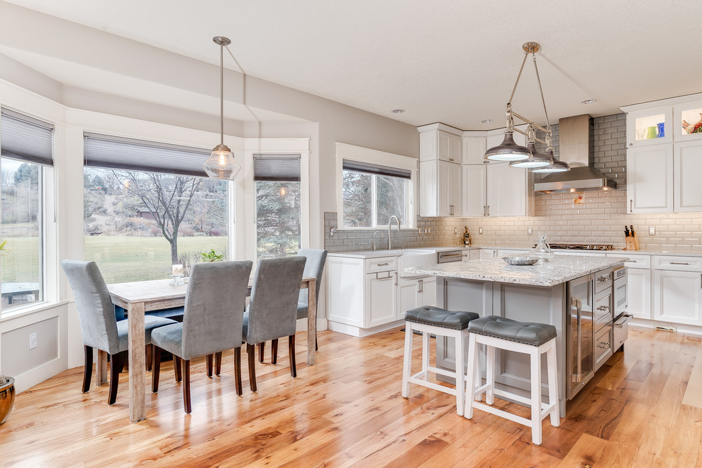 Mid-sized transitional u-shaped medium tone wood floor and brown floor eat-in kitchen photo in Boise with a farmhouse sink, shaker cabinets, white cabinets, quartz countertops, gray backsplash, subway tile backsplash, stainless steel appliances and an island