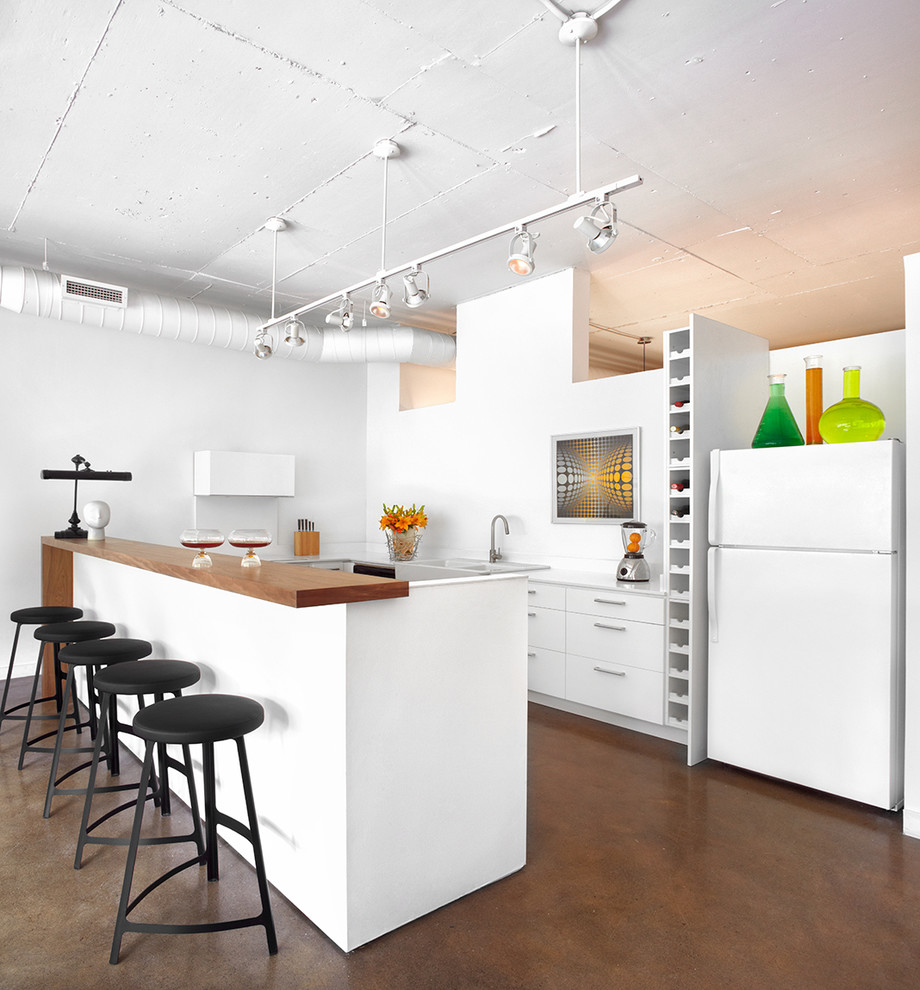 This is an example of an industrial u-shaped kitchen in Toronto with flat-panel cabinets, white cabinets, white appliances, concrete floors and a peninsula.