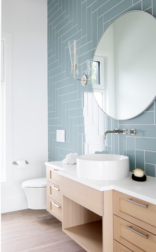 Design ideas for a mid-sized beach style 3/4 bathroom in Vancouver with recessed-panel cabinets, white cabinets, a wall-mount toilet, blue tile, glass tile, white walls, light hardwood floors, a vessel sink, engineered quartz benchtops, white benchtops, a single vanity and a floating vanity.