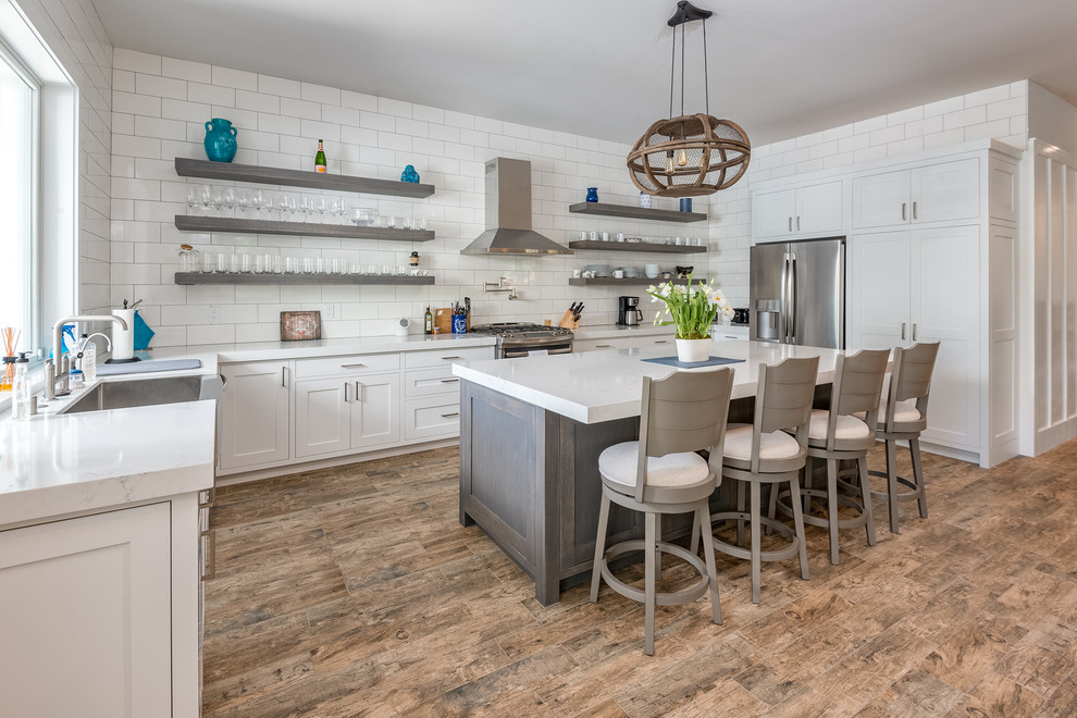 Country u-shaped kitchen in San Francisco with shaker cabinets, quartz benchtops, a farmhouse sink, white cabinets, white splashback, subway tile splashback, stainless steel appliances, with island, brown floor and white benchtop.