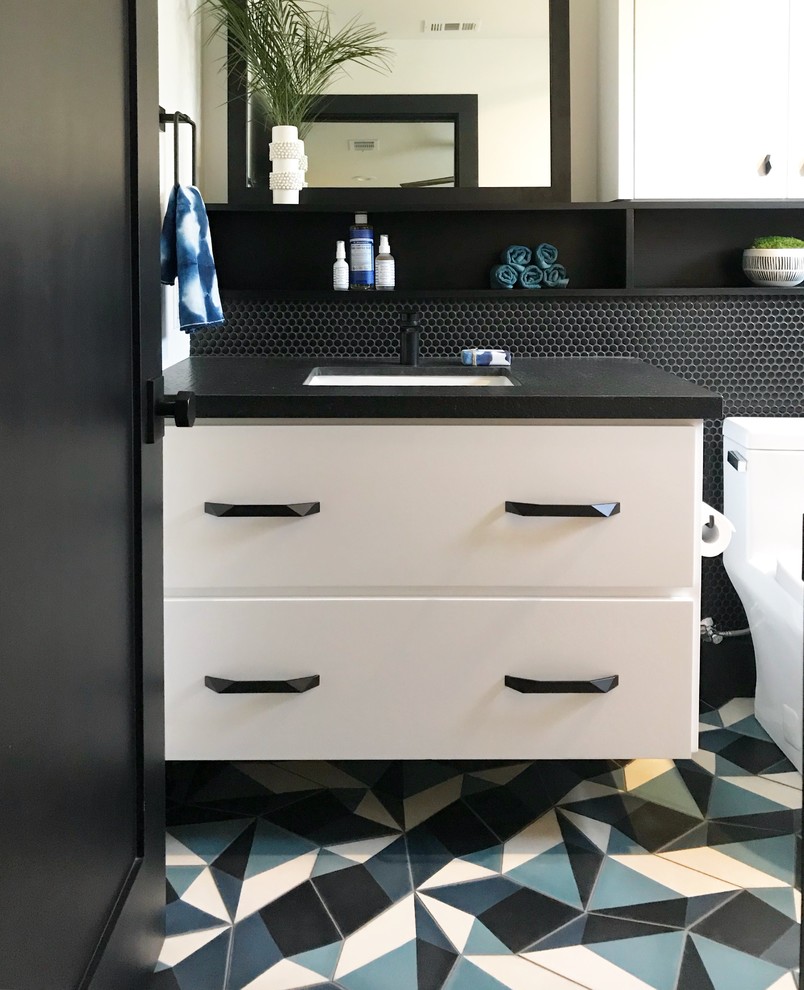Design ideas for a mid-sized transitional kids bathroom in Orange County with flat-panel cabinets, white cabinets, an alcove tub, a shower/bathtub combo, a one-piece toilet, black tile, cement tile, white walls, concrete floors, an undermount sink, granite benchtops, blue floor, a sliding shower screen and black benchtops.