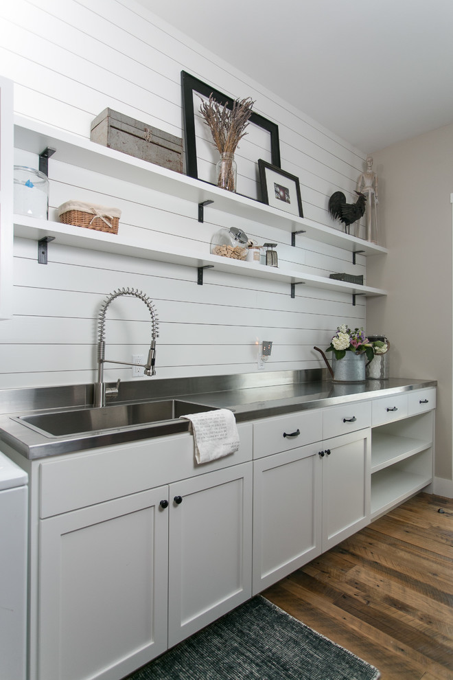 Country galley utility room in Austin with shaker cabinets, grey cabinets, stainless steel benchtops, beige walls, medium hardwood floors and a side-by-side washer and dryer.