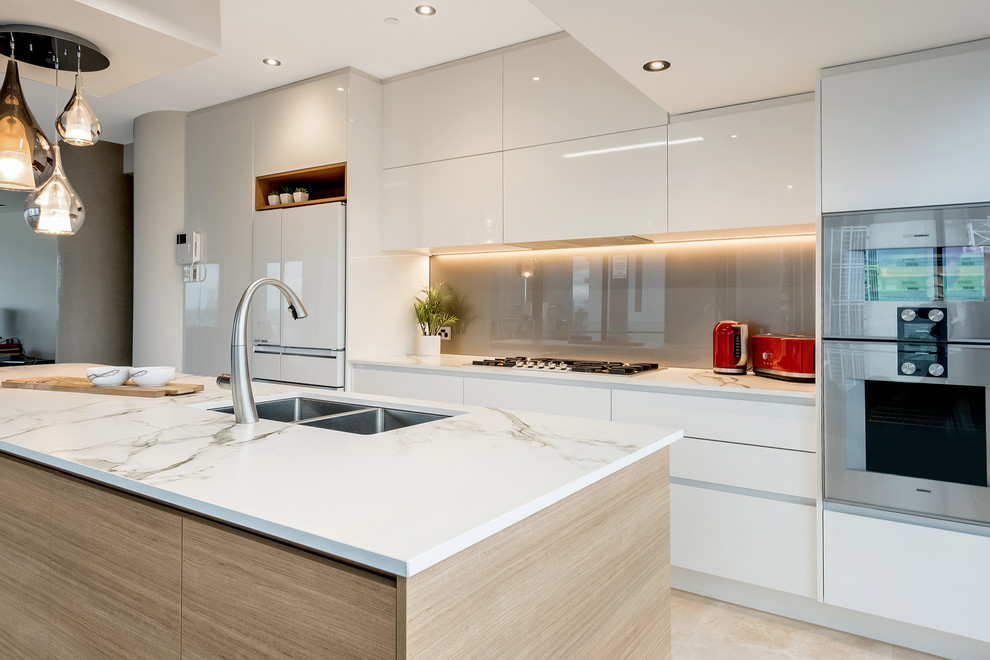 Mid-sized modern single-wall eat-in kitchen in Melbourne with flat-panel cabinets, white cabinets, quartz benchtops, brown splashback, glass sheet splashback, white appliances and with island.