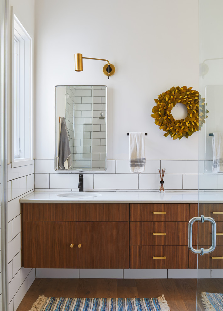 Scandinavian bathroom in Austin with flat-panel cabinets, medium wood cabinets, white tile, white walls, medium hardwood floors, an undermount sink, brown floor and white benchtops.