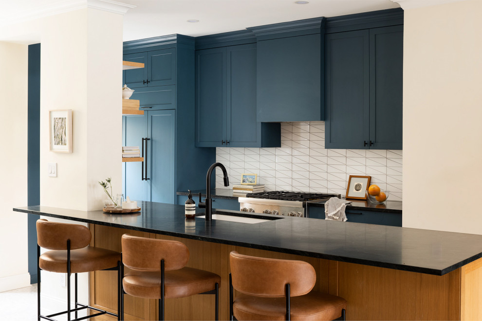 ニューヨークにある中くらいなトランジショナルスタイルのおしゃれなキッチン (アンダーカウンターシンク、シェーカースタイル扉のキャビネット、青いキャビネット、ソープストーンカウンター、白いキッチンパネル、セラミックタイルのキッチンパネル、パネルと同色の調理設備、コンクリートの床、白い床、黒いキッチンカウンター) の写真