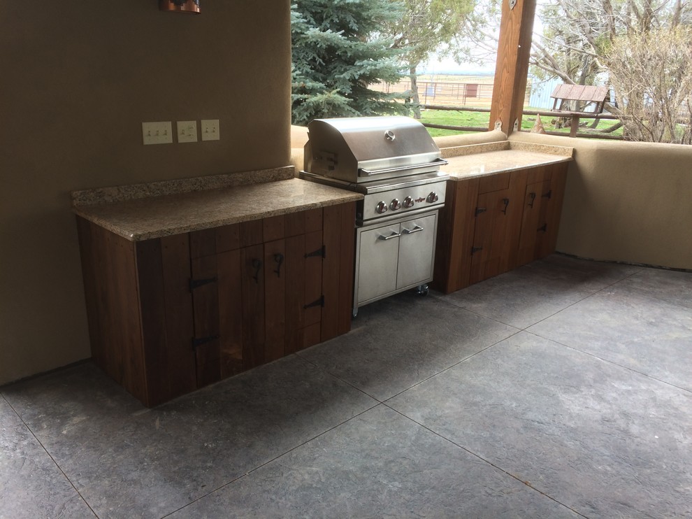 This is an example of a large backyard patio in Denver with an outdoor kitchen, stamped concrete and a roof extension.