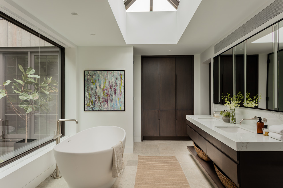 Design ideas for a contemporary master bathroom in Boston with flat-panel cabinets, dark wood cabinets, a freestanding tub, white walls, an undermount sink, beige floor, white benchtops and a double vanity.