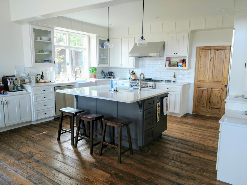 Mountain style galley dark wood floor and brown floor kitchen photo with a farmhouse sink, recessed-panel cabinets, white cabinets, quartzite countertops, white backsplash, subway tile backsplash, stainless steel appliances, an island and white countertops
