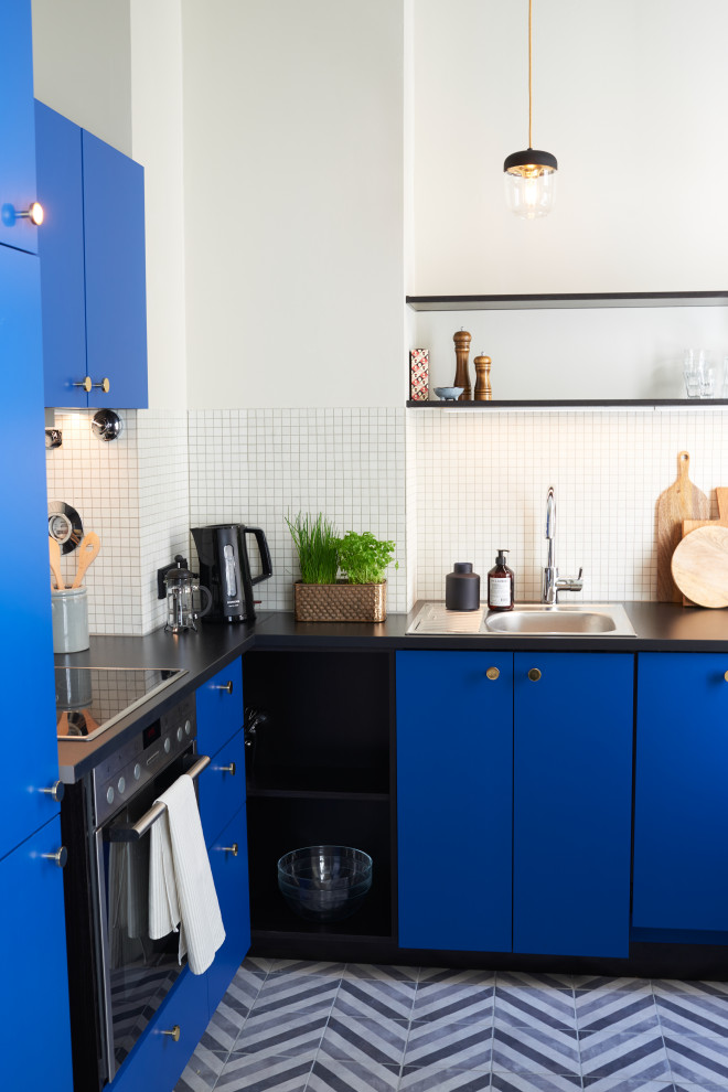 This is an example of a small scandinavian l-shaped open plan kitchen in Berlin with a single-bowl sink, flat-panel cabinets, blue cabinets, laminate benchtops, beige splashback, mosaic tile splashback, stainless steel appliances, cement tiles, no island, grey floor and black benchtop.