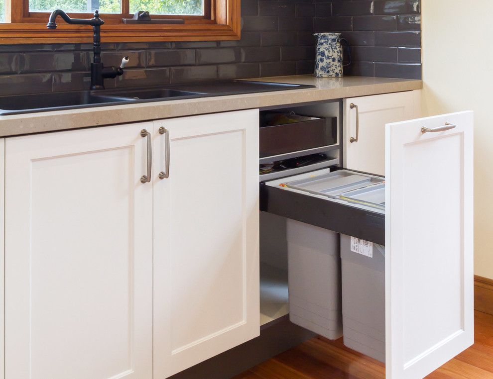 This is an example of a large transitional l-shaped eat-in kitchen in Melbourne with a drop-in sink, shaker cabinets, white cabinets, grey splashback, subway tile splashback, black appliances, medium hardwood floors and with island.