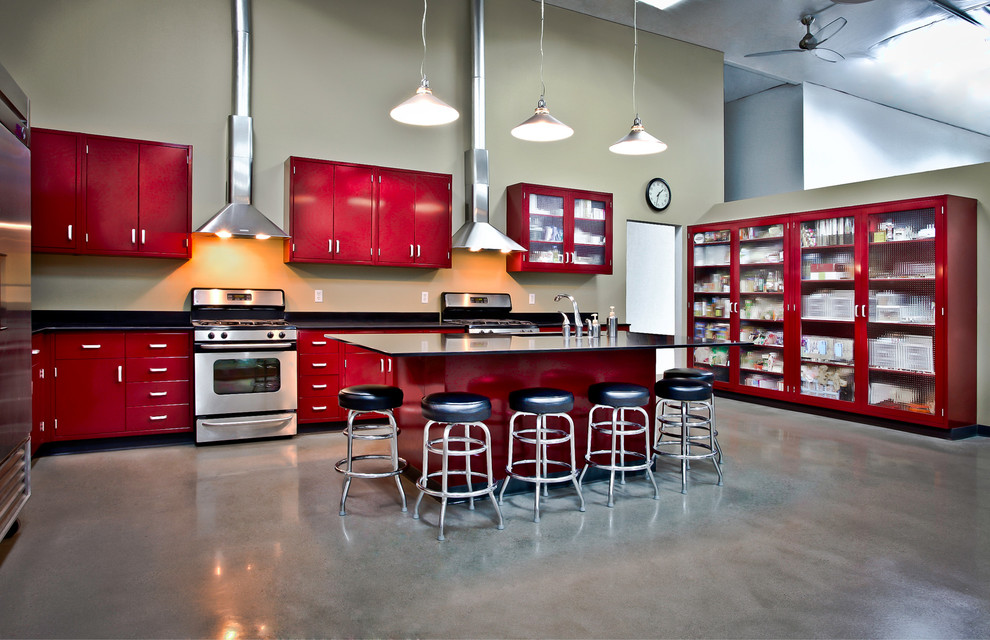 Photo of an industrial l-shaped kitchen in Orange County with stainless steel appliances, red cabinets and flat-panel cabinets.