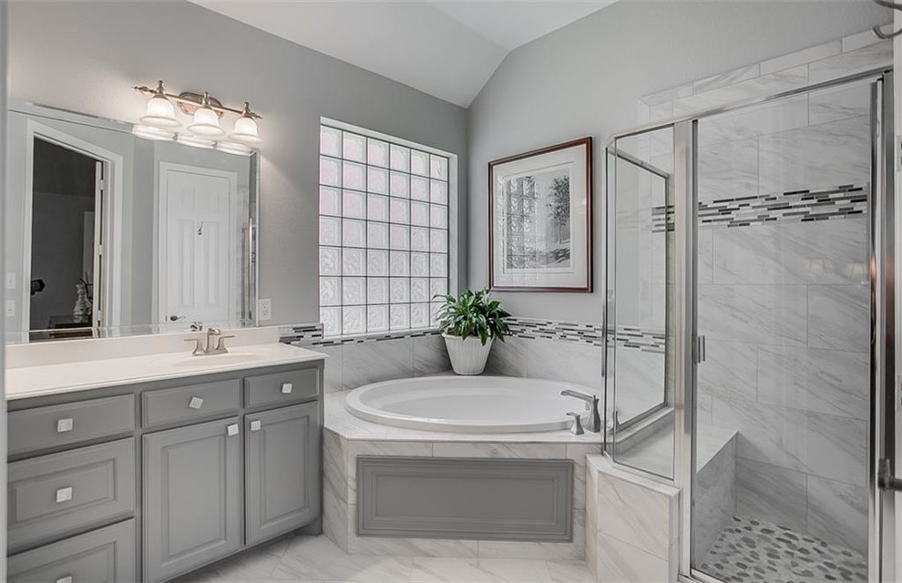 This is an example of a mid-sized tropical master bathroom in Dallas with raised-panel cabinets, grey cabinets, a corner tub, a corner shower, black and white tile, gray tile, multi-coloured tile, white tile, marble, grey walls, marble floors, an undermount sink, white floor, a hinged shower door and white benchtops.