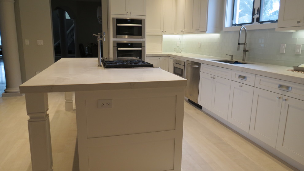 Enclosed kitchen - large transitional l-shaped light wood floor and beige floor enclosed kitchen idea with a double-bowl sink, shaker cabinets, white cabinets, marble countertops, blue backsplash, glass tile backsplash, stainless steel appliances and an island