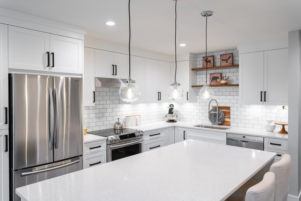 Photo of a mid-sized transitional l-shaped eat-in kitchen in Vancouver with an undermount sink, white cabinets, quartz benchtops, white splashback, subway tile splashback, stainless steel appliances, with island, brown floor, white benchtop, shaker cabinets and vinyl floors.