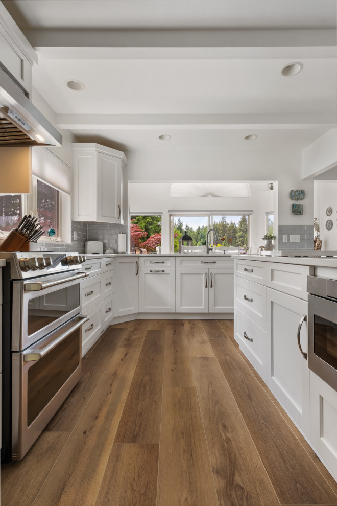 Inspiration for a mid-sized beach style galley eat-in kitchen in Seattle with a drop-in sink, beaded inset cabinets, white cabinets, marble benchtops, grey splashback, ceramic splashback, stainless steel appliances, vinyl floors, multiple islands, brown floor, white benchtop and coffered.
