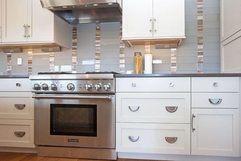 Example of a large transitional l-shaped medium tone wood floor eat-in kitchen design in Boston with an undermount sink, shaker cabinets, white cabinets, quartz countertops, gray backsplash, glass sheet backsplash, stainless steel appliances and an island