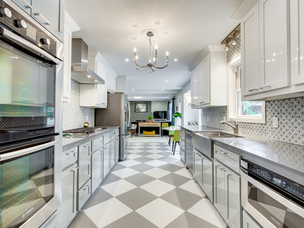 This is an example of a transitional galley separate kitchen in Oklahoma City with a farmhouse sink, shaker cabinets, grey cabinets, concrete benchtops, grey splashback, stainless steel appliances, no island and multi-coloured floor.